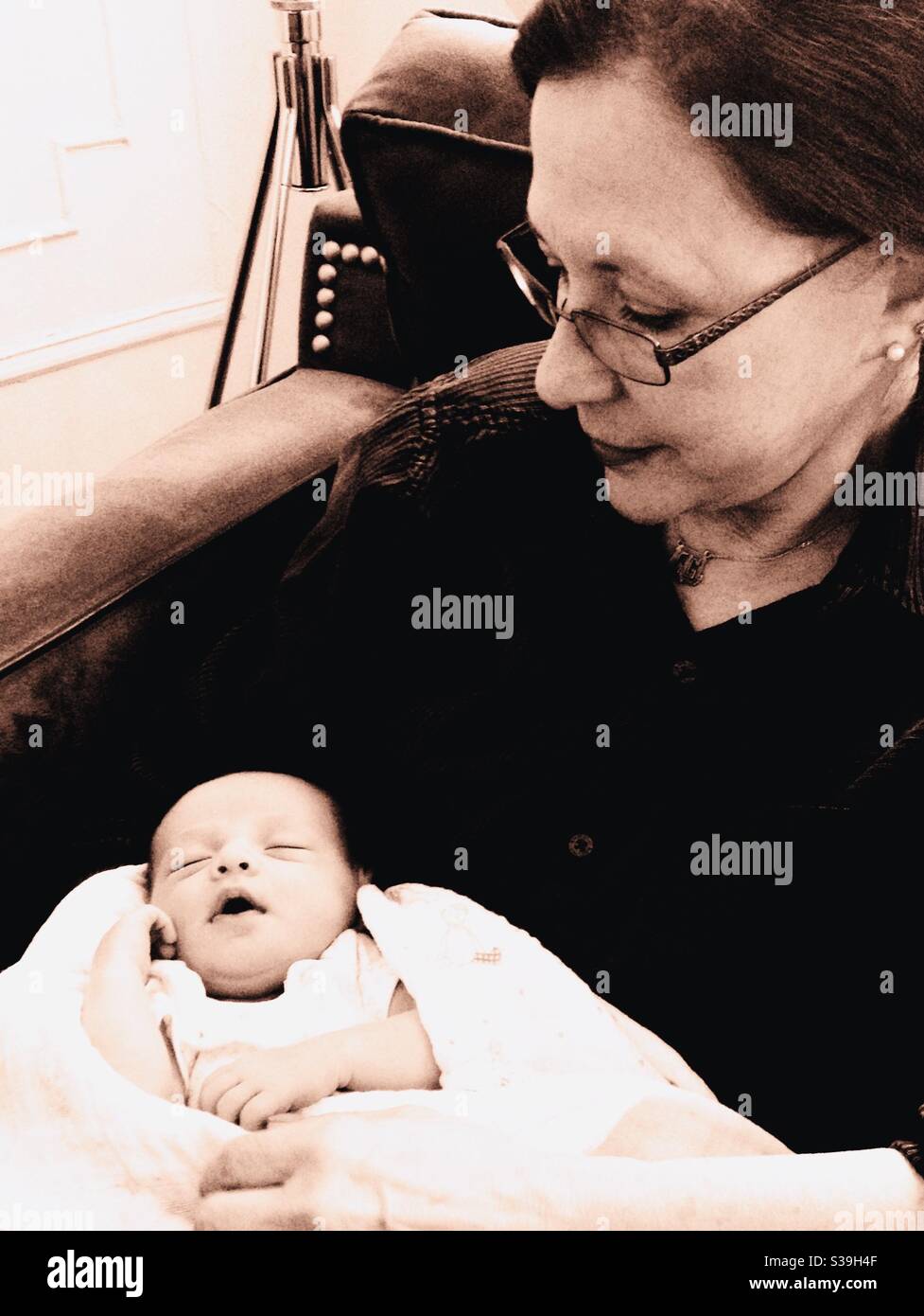 Junge Großmutter hält ihr neugeborenes Enkelkind. - Smartphone-aufgenommenes Stockfoto