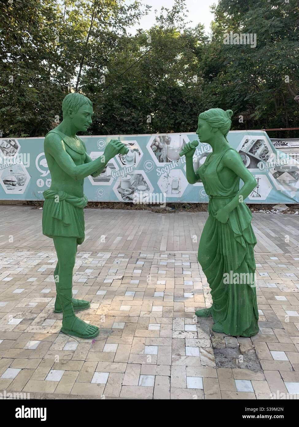 Zwei grüne Statuen eines Mannes, der eine singende Frau filmt Stockfoto