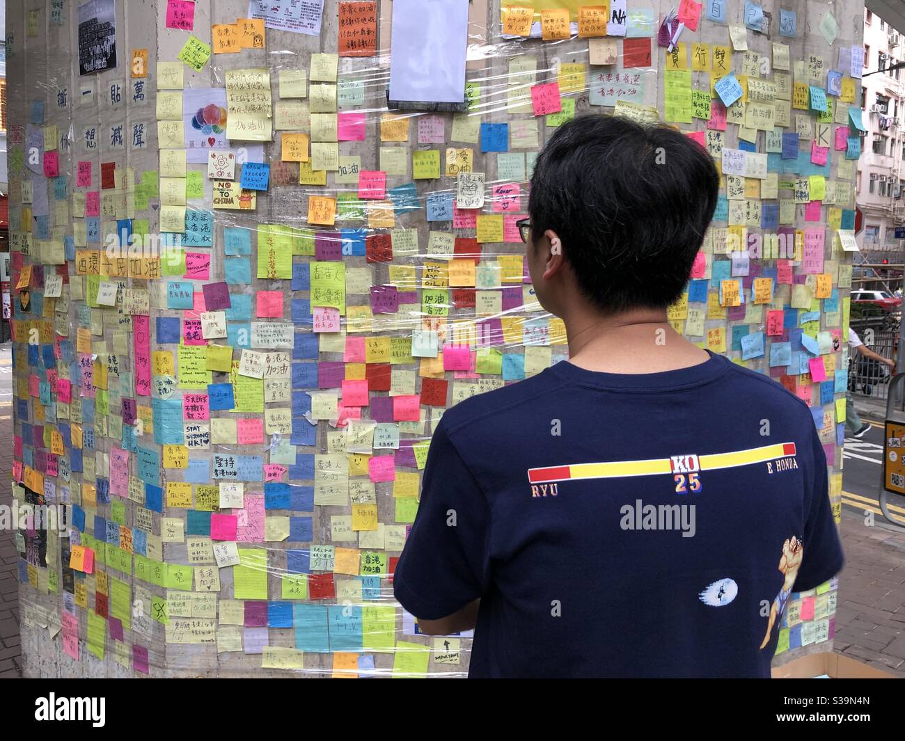 Ein junger Mann liest einige der Tausenden von Nachrichten, die auf bunten Post-it-Notizen zur Unterstützung der prodemokratischen Proteste in Hongkong hinterlassen wurden. Stockfoto