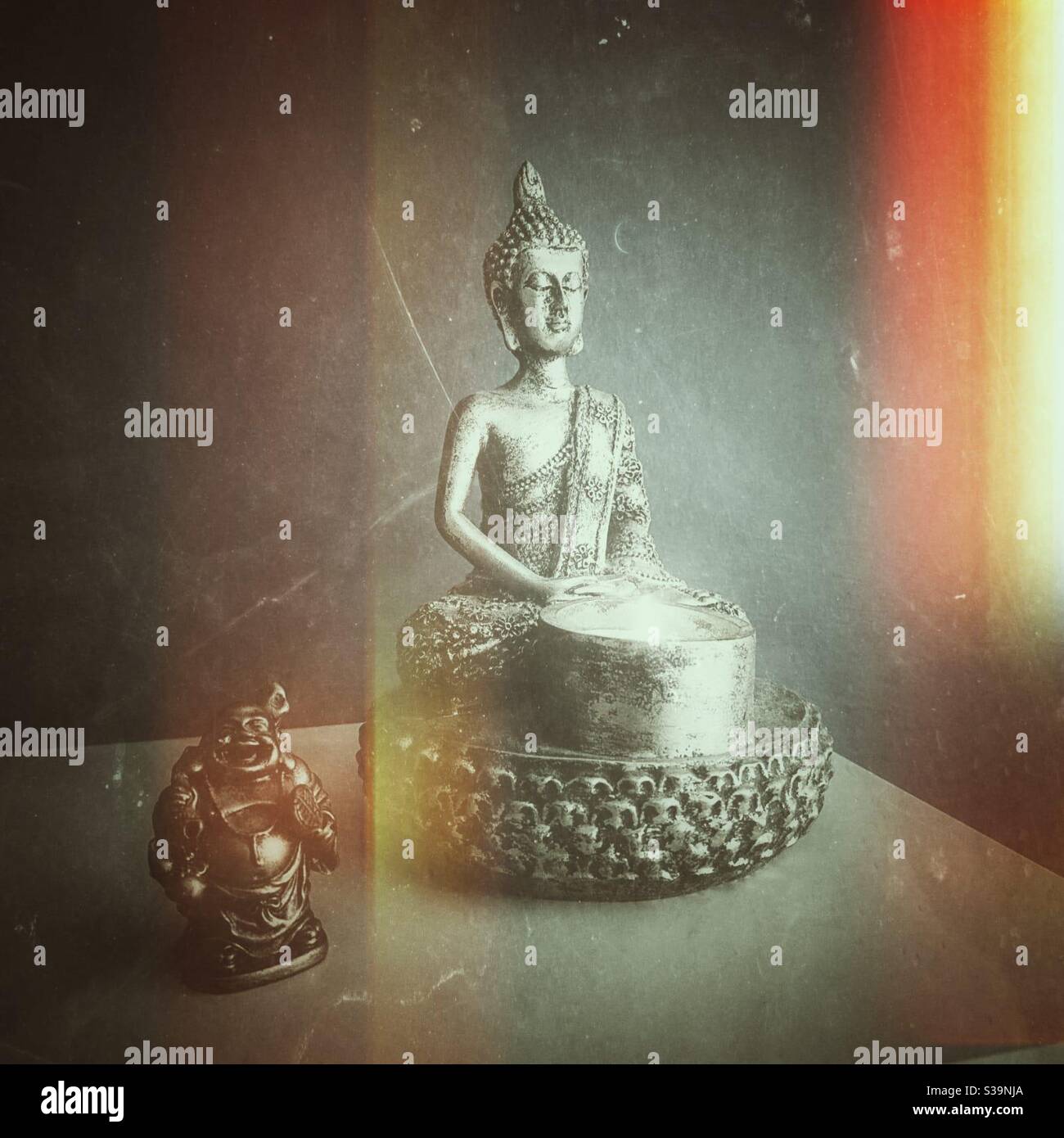 Ein Foto von zwei Buddha-Statuen mit einer brennenden Kerze und Lichtreflexfilter hinzugefügt. - Smartphone-aufgenommenes Stockfoto