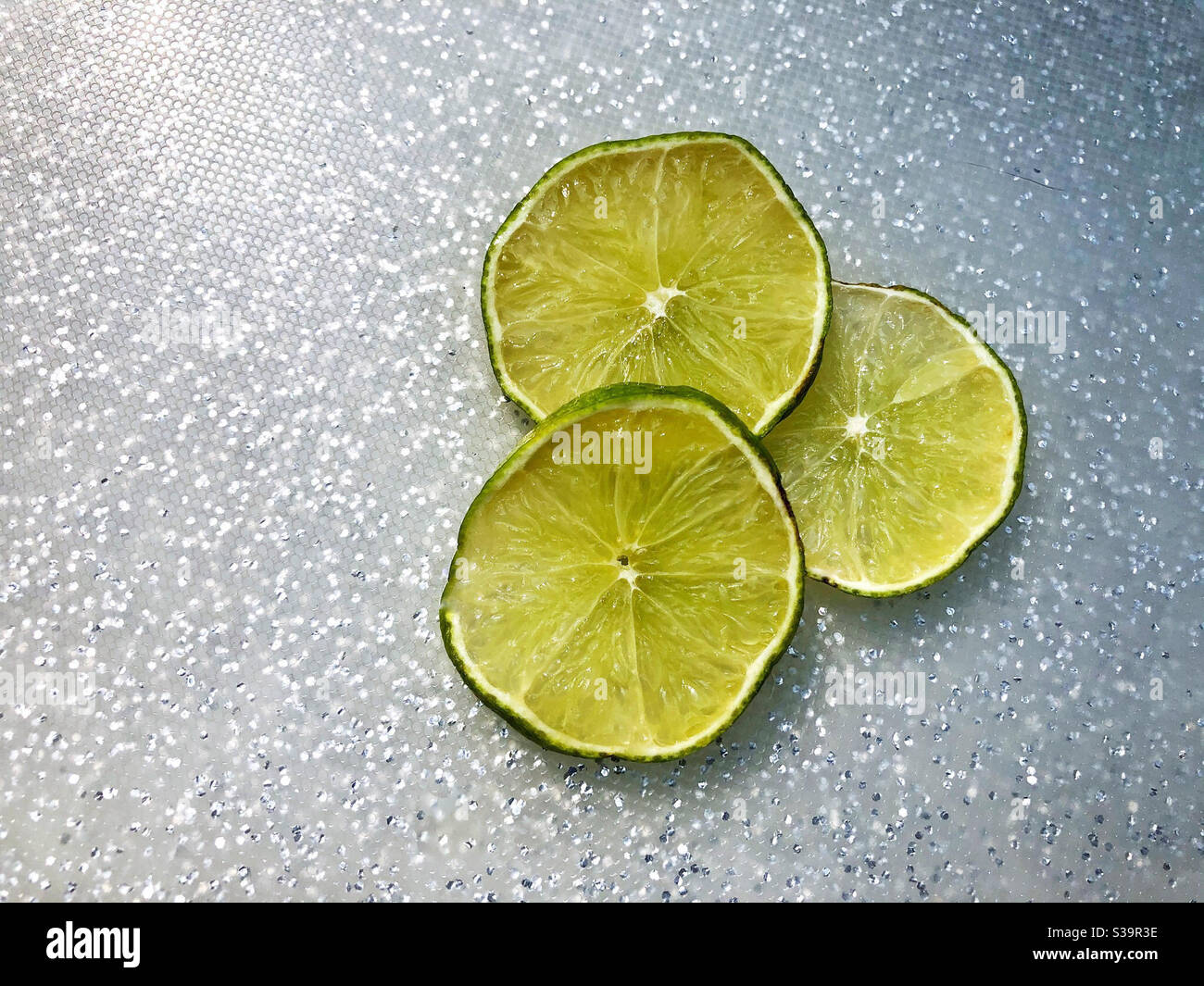 Limettenscheiben für Getränke auf glitzerndem silbernen Glitzer-Schneidebrett Stockfoto
