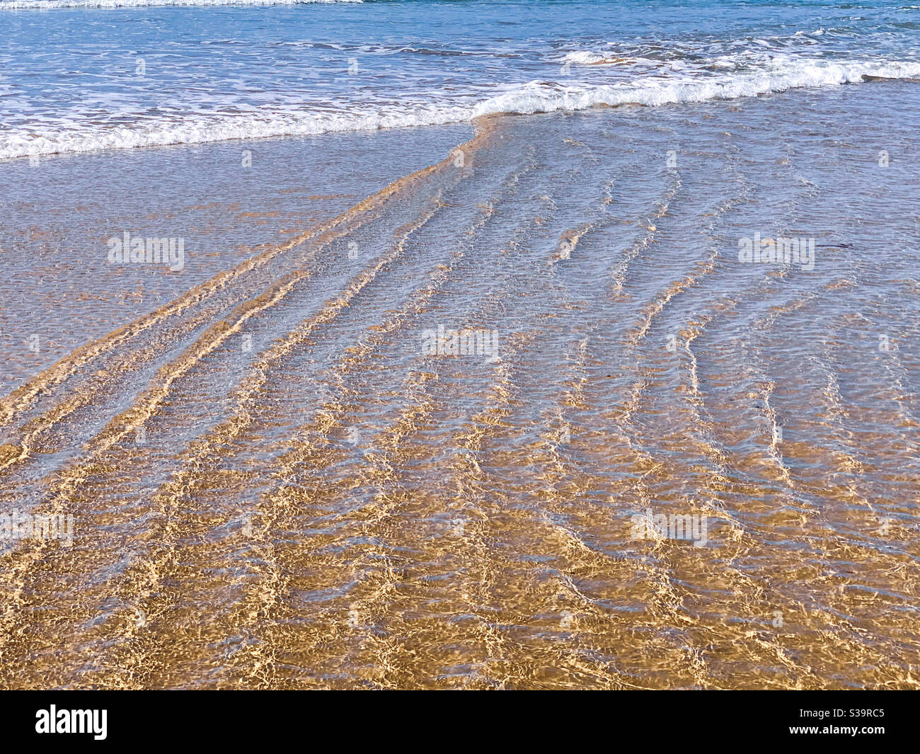 Muster im nassen Strandsand, der durch Meerwasser und Wellen gebildet wird, schaumig an den Rändern, Linien und Wellen Stockfoto