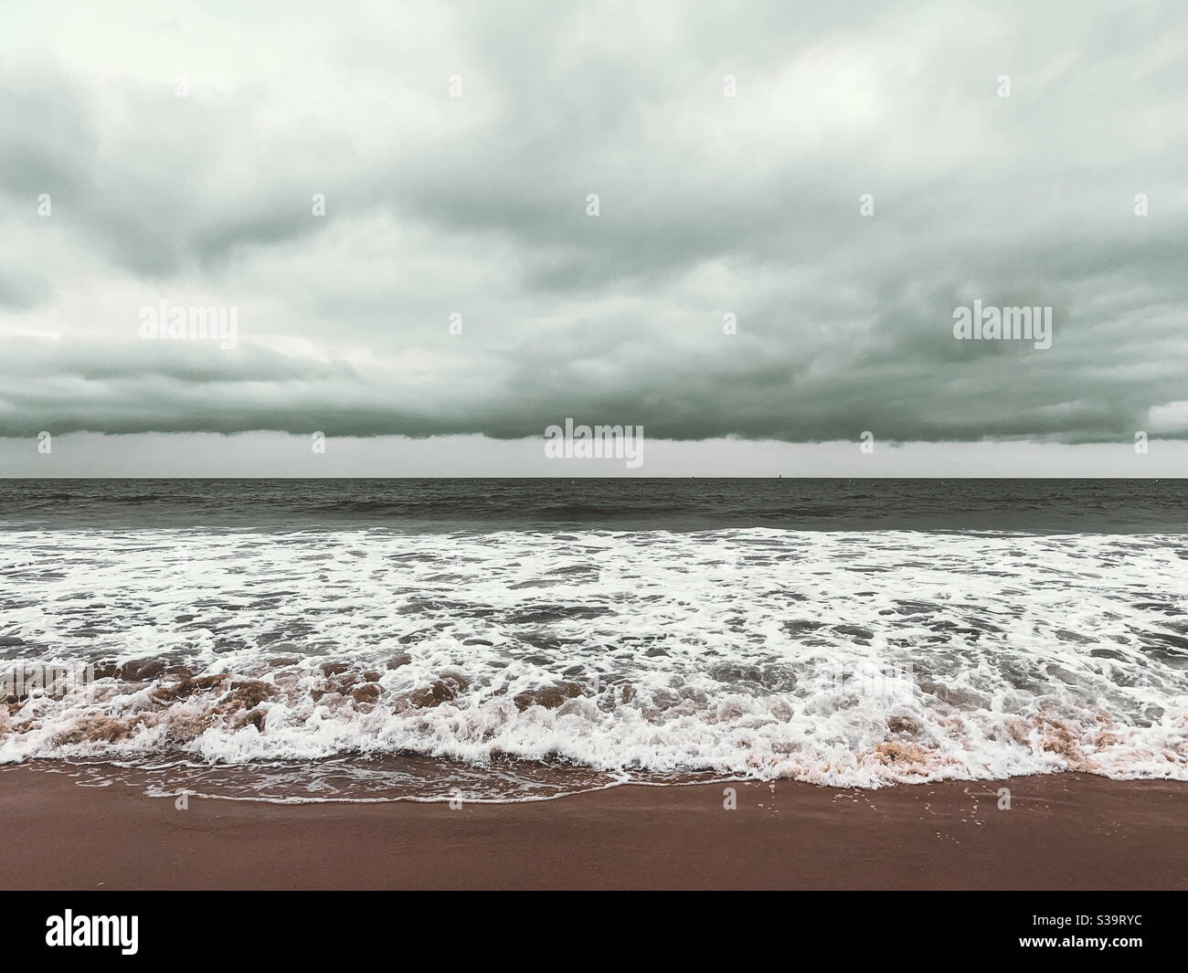 Seascape mit niedrig liegender Wolkendecke. Meereswellen waschen sich an einem bewölkten Tag auf den Sandstrand. Stockfoto