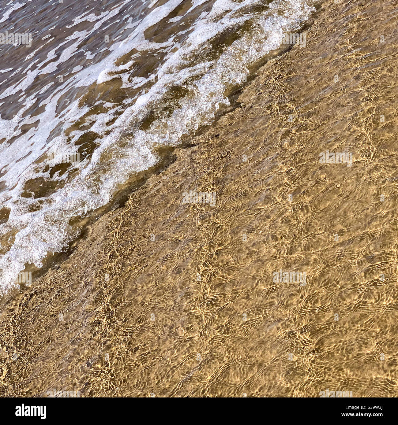 Muster im Sand, Meerwasser, das auf den Strand wascht, kleine Wellen, die Schaum machen, diagonale Perspektive Stockfoto