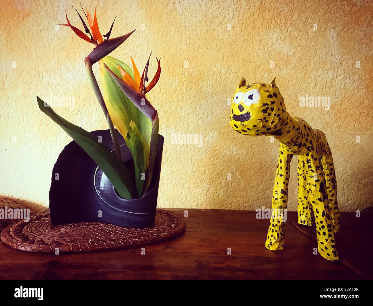 Ein Paradiesvogel Blume und ein Papiermaché handgefertigten jaguar schmücken ein Haus mit einer gelben Wand in Coyoacan, Mexiko-Stadt, Mexiko - Smartphone-aufgenommenes Stockfoto