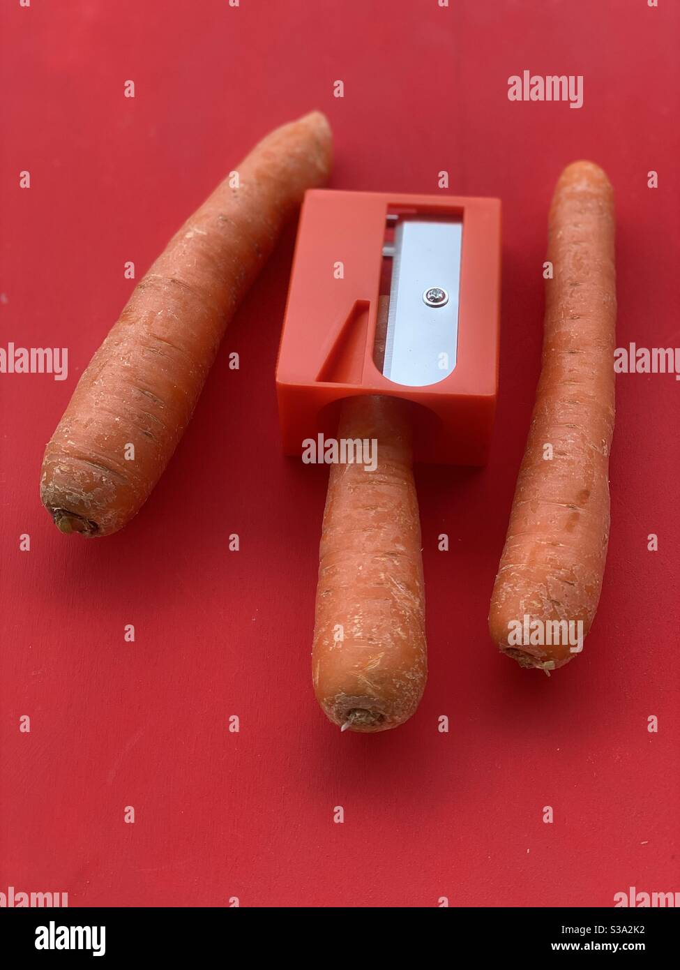 Karotten mit einem Karottenspitzer über einem hölzernen roten Brett Stockfoto