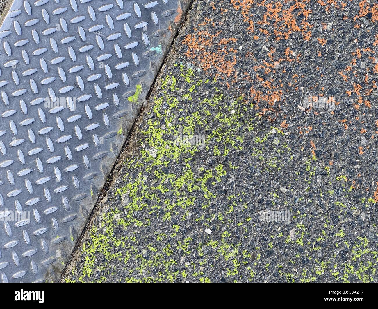 Nahaufnahme auf gemustertem Metall neben Asphalt mit orange und grün lackiert, Schaffung texturierter Hintergrund geeignet für Compositing und Grafiken - Smartphone-aufgenommenes Stockfoto