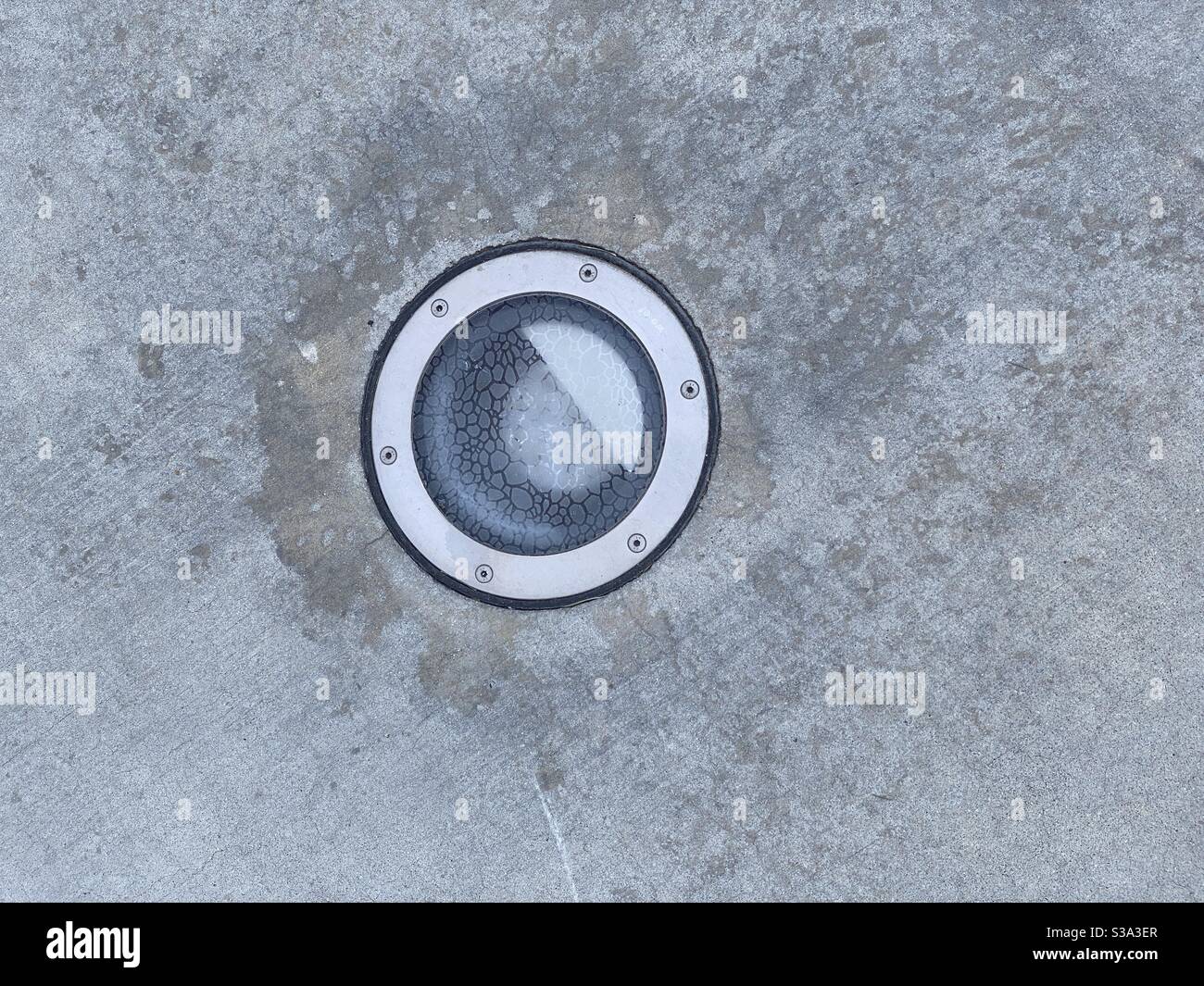 Detail des Lichts mit texturierter Glasabdeckung, eingebettet in Beton Bürgersteig, schaffen abstrakte Hintergrundtextur - Smartphone-aufgenommenes Stockfoto