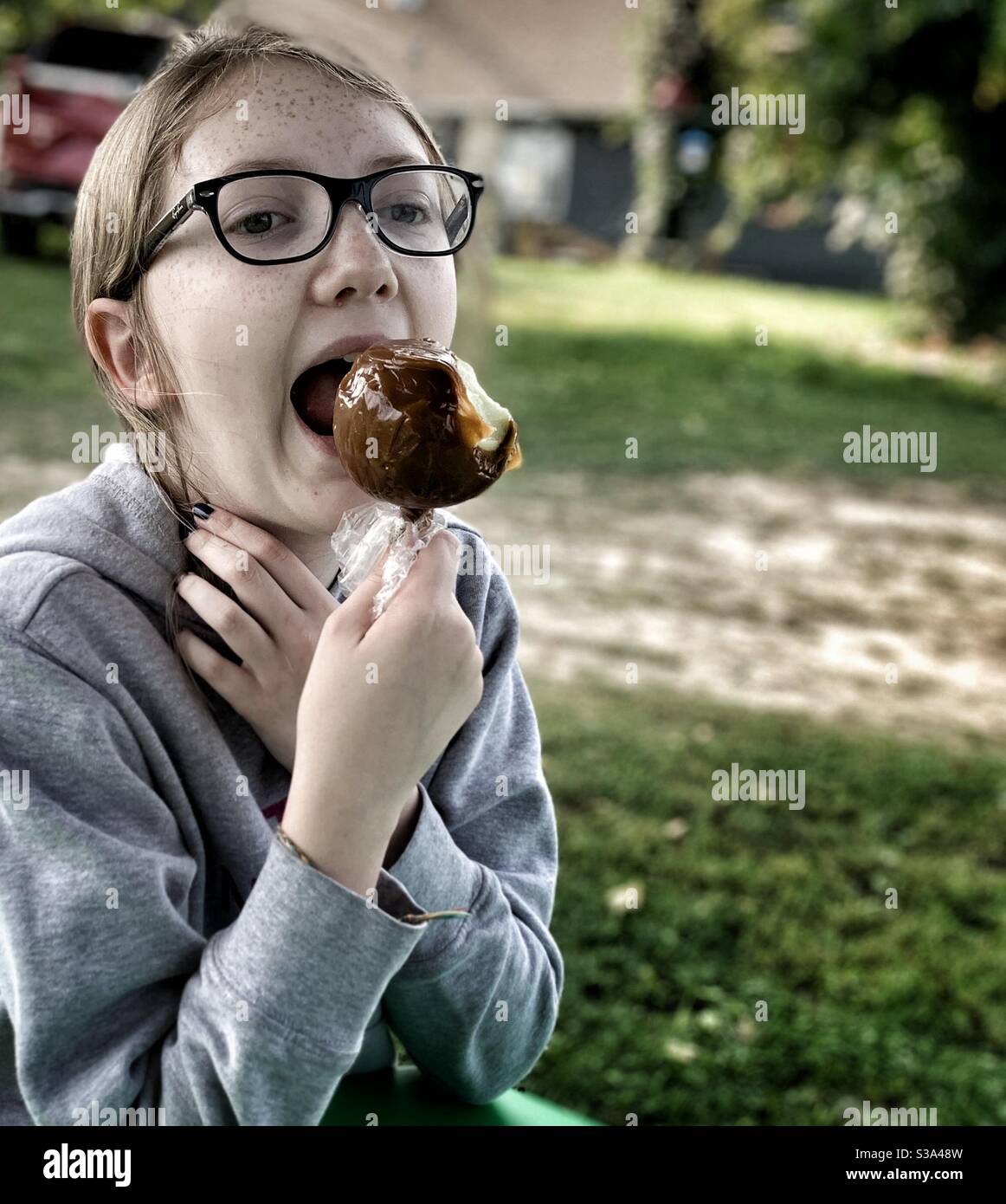 DUBUQUE, IOWA, September 2020 --Portrait-Foto des jungen kaukasischen Mädchens, das an einem sonnigen Herbsttag in einen leckeren Karamellapfel beißt. Stockfoto