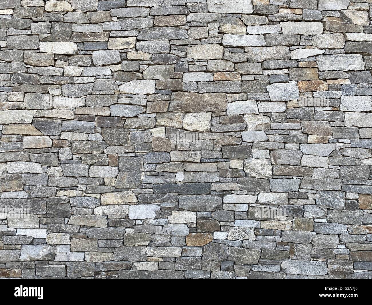 Wand aus seltsam geformten, grauen und anderen erdfarbenen Ziegeln aus Stein, Schaffung abstrakter Hintergrundtextur geeignet für Compositing - Smartphone-aufgenommenes Stockfoto