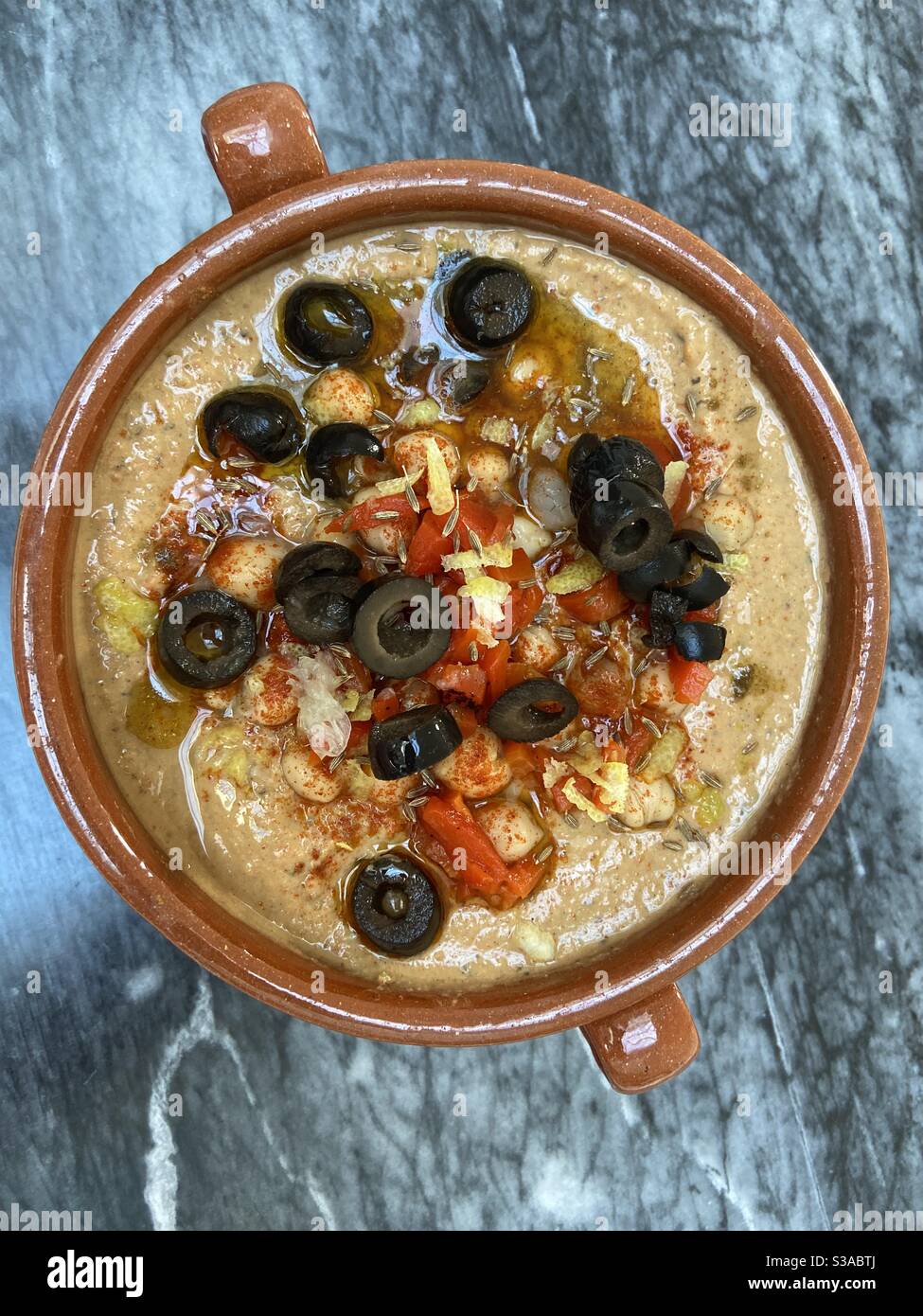 Hausgemachter Humus mit Oliven, gerösteten Paprika, geräuchertem Paprika und Zitronenschale. Stockfoto