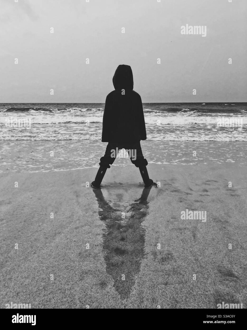 Silhouette eines Jungen, der am Strand steht und auf stürmisches Meer blickt. Stockfoto