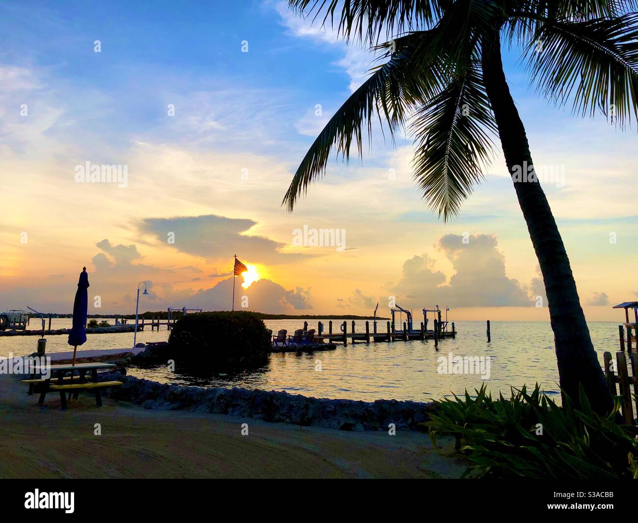 Sonnenuntergang über dem Wasser an einem Pier mit einer Palme und einer US-Flagge. Stockfoto