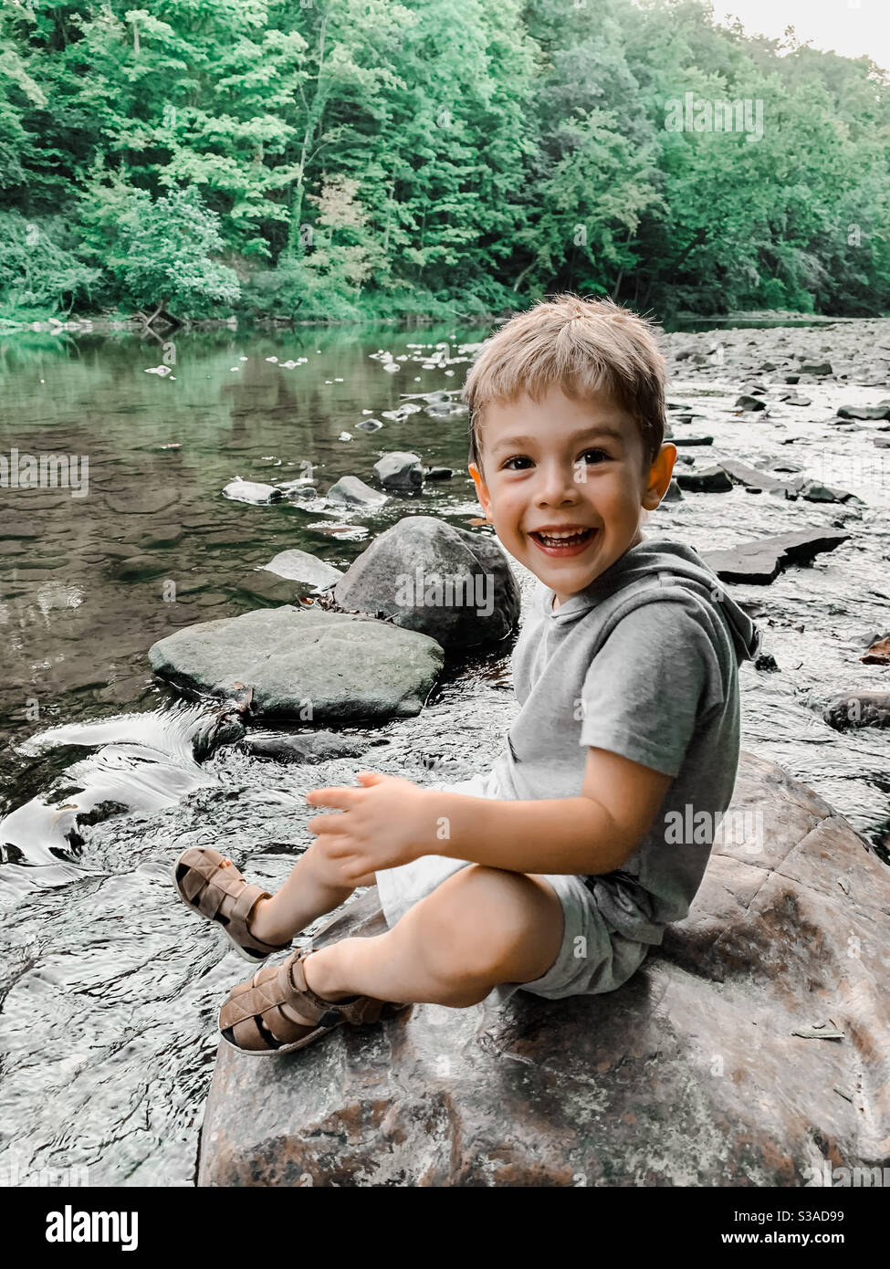 Junge lächelt, während er auf dem Flussbett sitzt Stockfoto