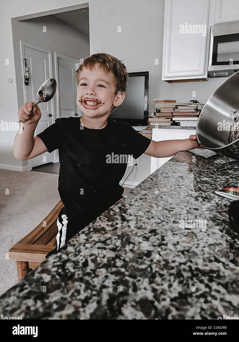 Junge leckt den Löffel und macht Brownies in der Küche Stockfoto