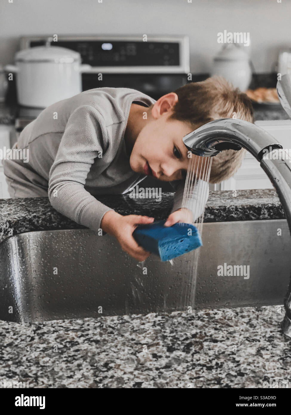 Junge versucht, Geschirr zu waschen Stockfoto