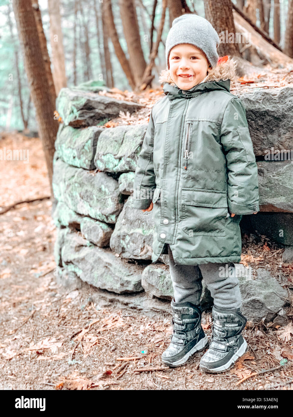 Ein kleines 4-jähriges Kind, das gegen Ende des Winters 2020 im Park unterwegs ist und von einer runden Figur aus Felsen fotografiert wird. Stockfoto