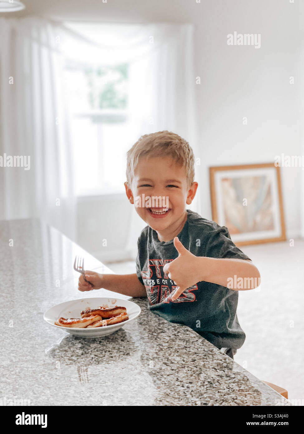 Ein kleiner blonder Junge, der Pfannkuchen zum Frühstück in einem guten Essen isst Stimmung Stockfoto