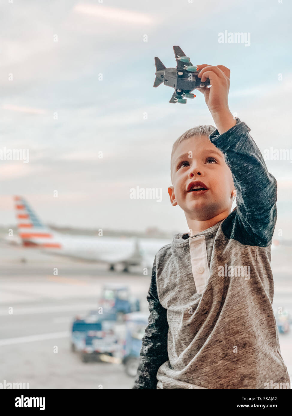 Kleiner blonder Junge, der nach einem internationalen Flug nach Hause zurückkehrt und am Flughafen mit einem Spielzeugflugzeug spielt Stockfoto