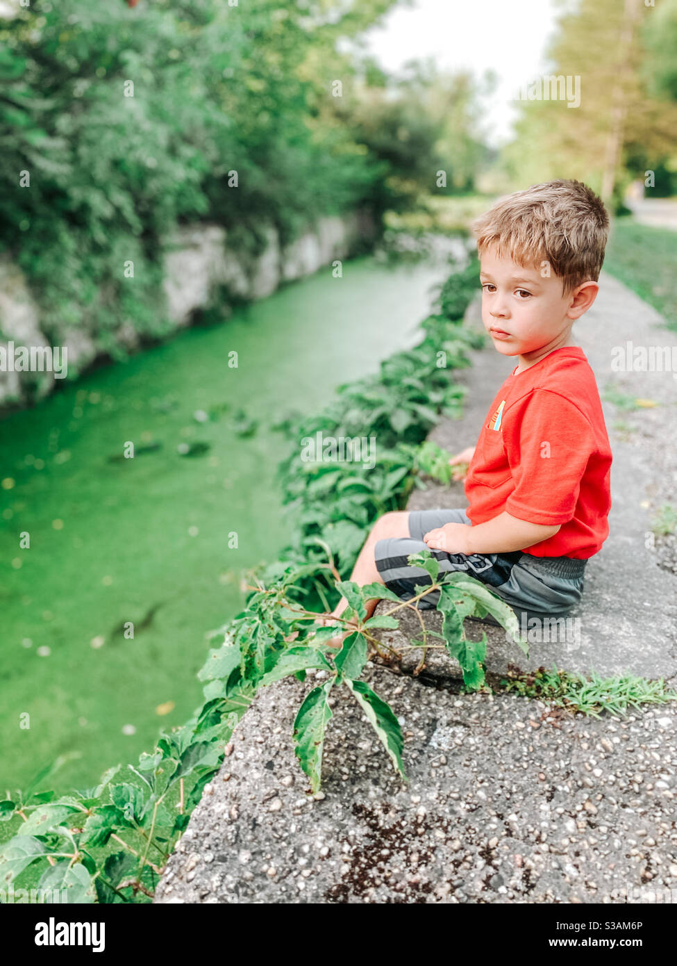 Einsamer Junge, der auf der Steinmauer sitzt und in einen Sumpf geht. Stockfoto
