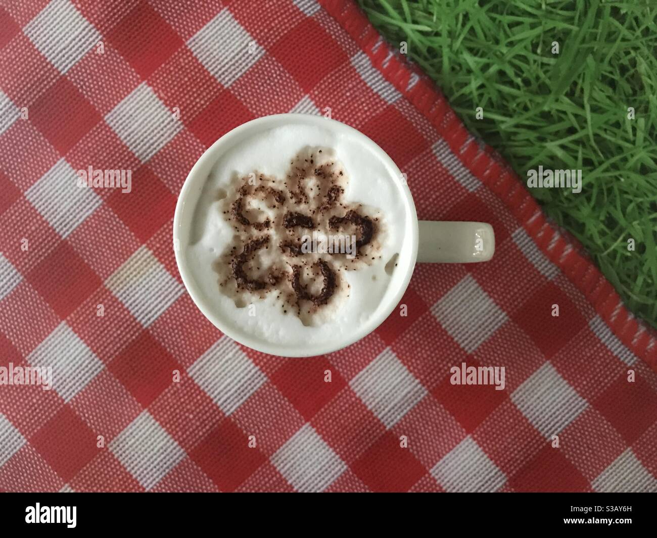 Blume geformtes Design auf einer Tasse Cappuccino-Kaffee - Smartphone-aufgenommenes Stockfoto