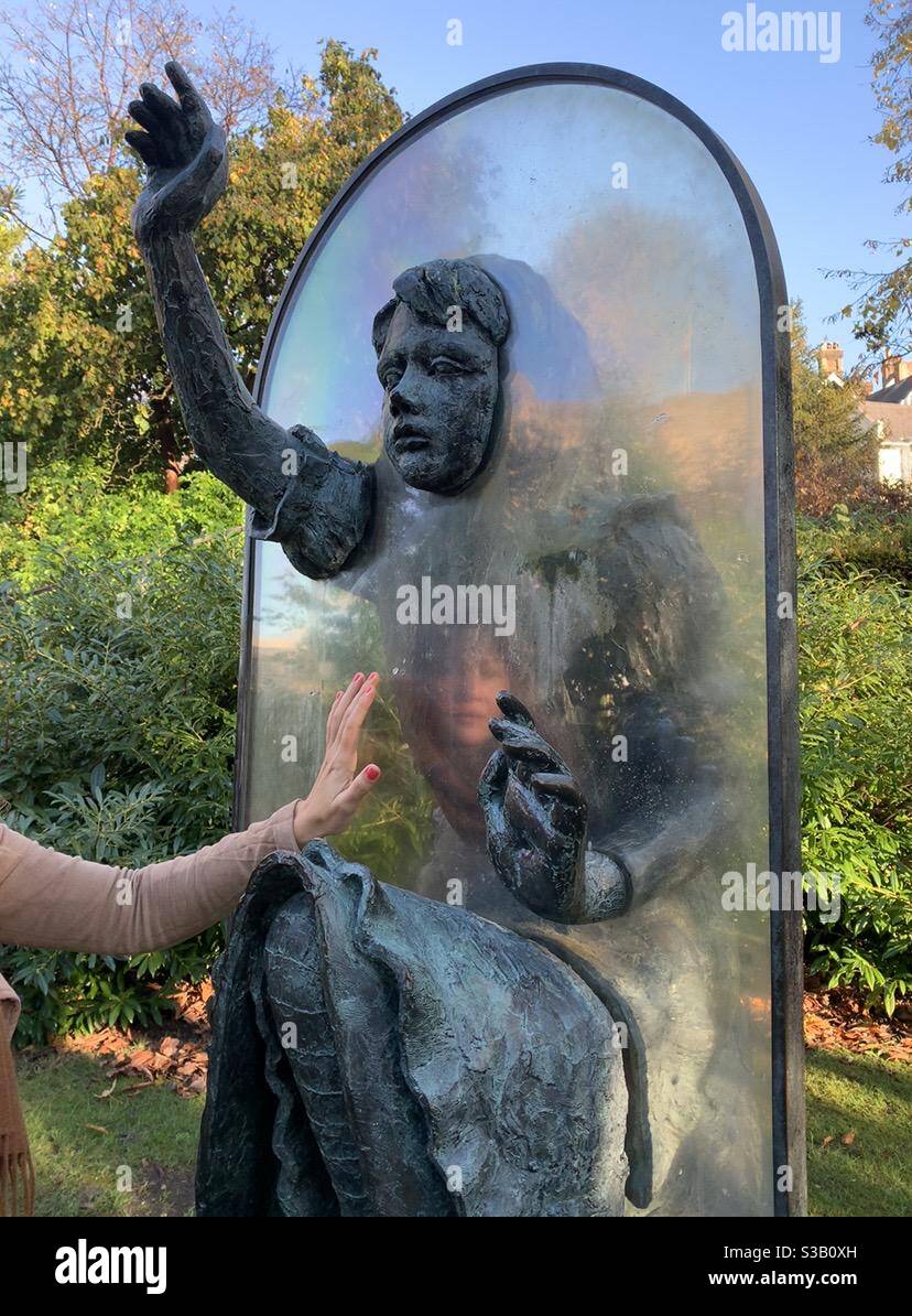 Das Gesicht der Frau spiegelt sich in Alice durch die Glasstatue Guildford Stockfoto