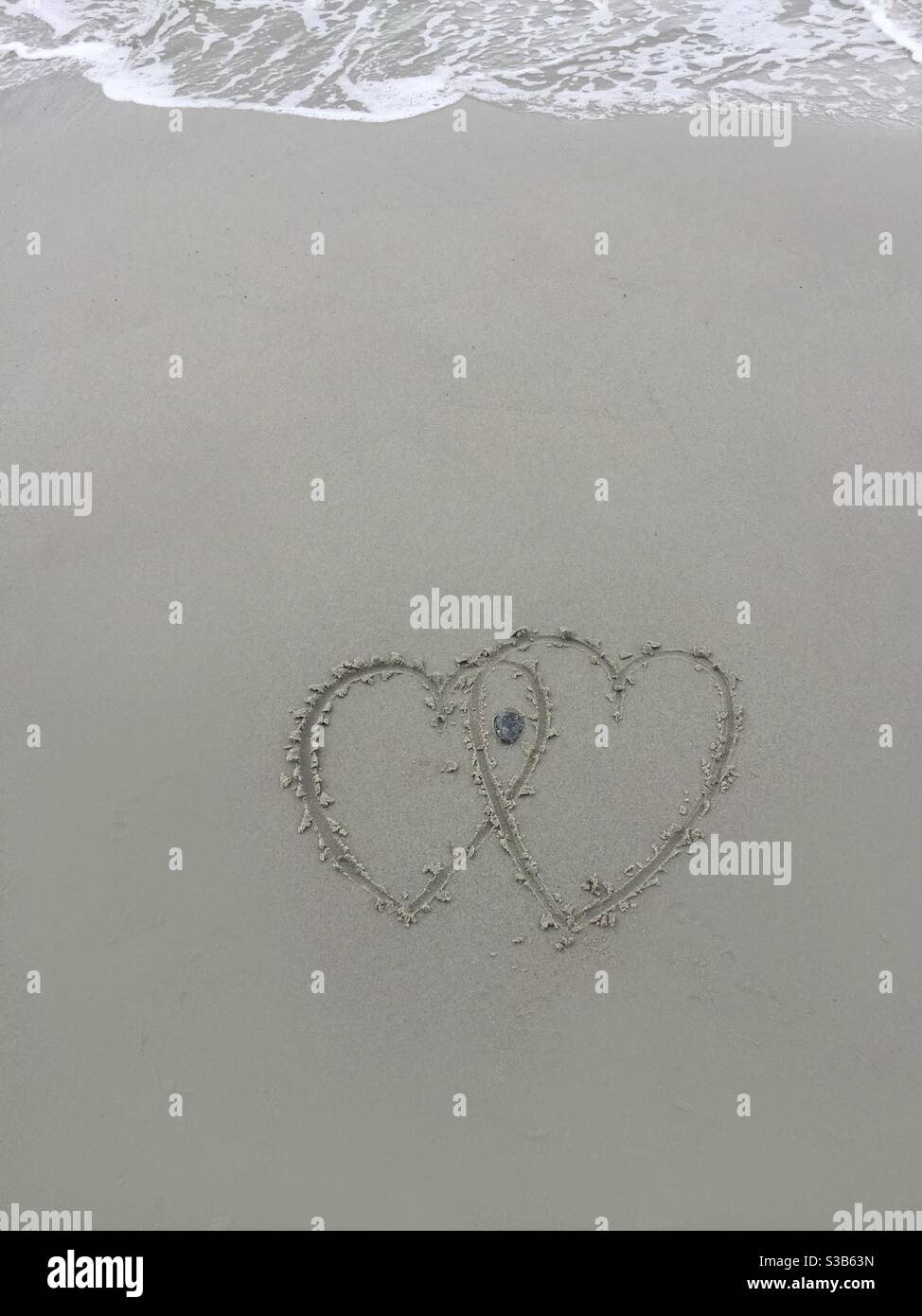 Herzen im Sand, aber nicht lange. Eingehende Kurven werden überspült und die Zeichnung in kurzer Reihenfolge gelöscht. Diese Kunst ist nicht lang und die Zeit vergeht. - Smartphone-aufgenommenes Stockfoto