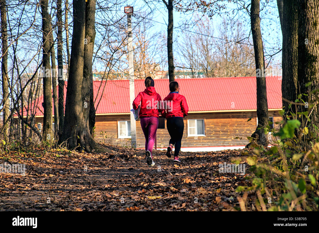 Zwei Mädchen in Rot joggen zwischen Bäumen im Park Stockfoto