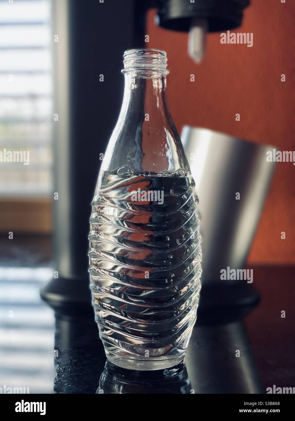 Glas Sodastream Flasche mit kohlensäurehaltigen Wasser vor der Sodastream Maschine in einer modernen Küche. Stockfoto
