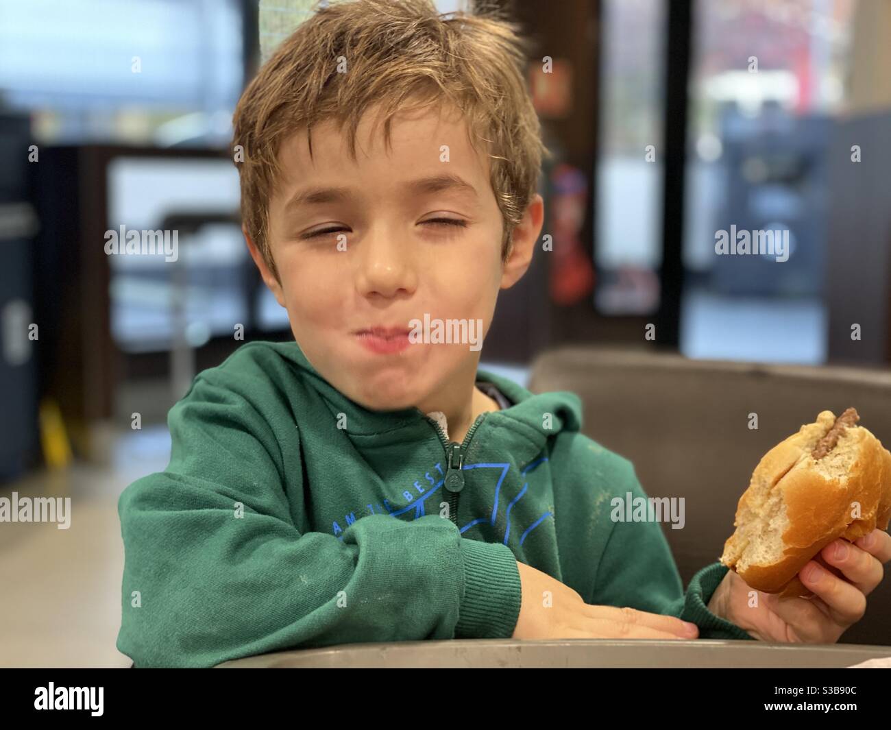 Hungrige junge Burger essen - Smartphone-aufgenommenes Stockfoto