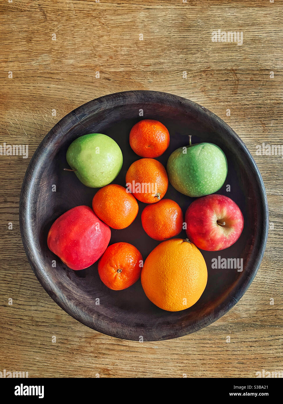 Ein Blick von oben auf eine hölzerne Obstschale mit Äpfeln, Mandarinen und einer Orange. Viele gesunde Lebensmittel inc. Vitamin C. Foto ©️ COLIN HOSKINS. Stockfoto