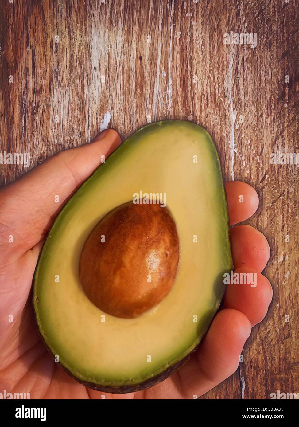 Hand hält eine Avocado-Hälfte. Frische Lebensmittel und eine gesunde Ernährung - Smartphone-aufgenommenes Stockfoto