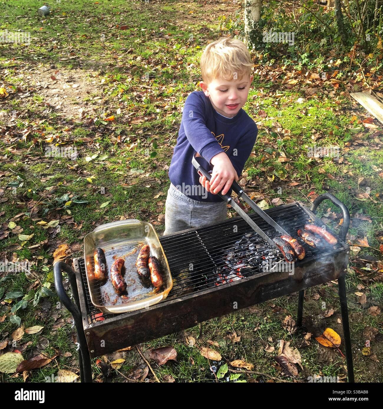 Vier Jahre alter Junge kocht Würstchen auf einem Grill. Stockfoto