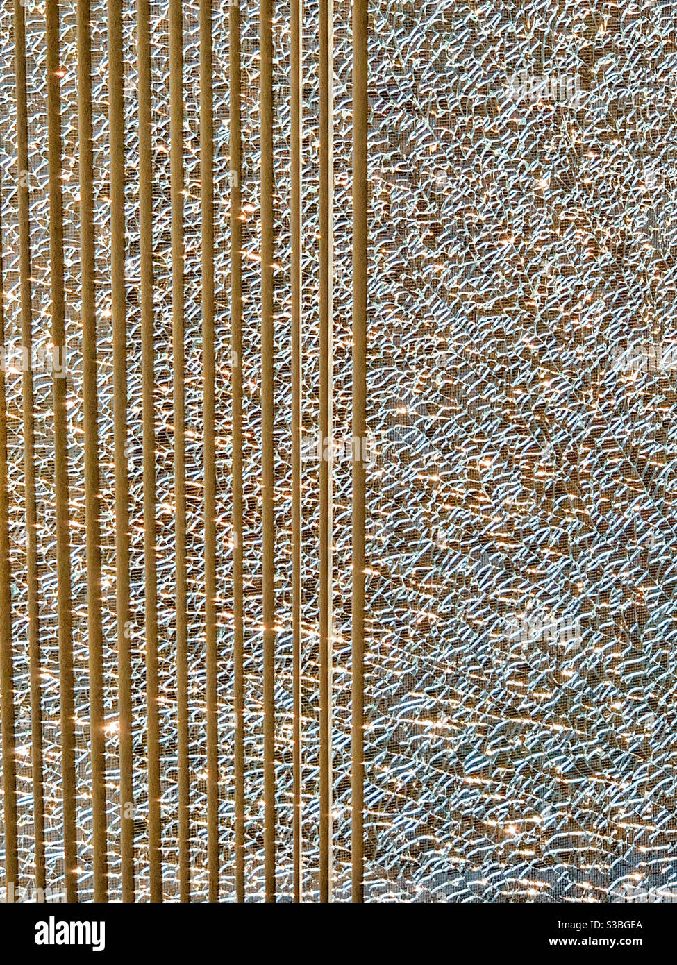 Vertikale Linien, zerbrochenes Glas mit goldenen Brechungen und vertikalen Jalousien - Smartphone-aufgenommenes Stockfoto