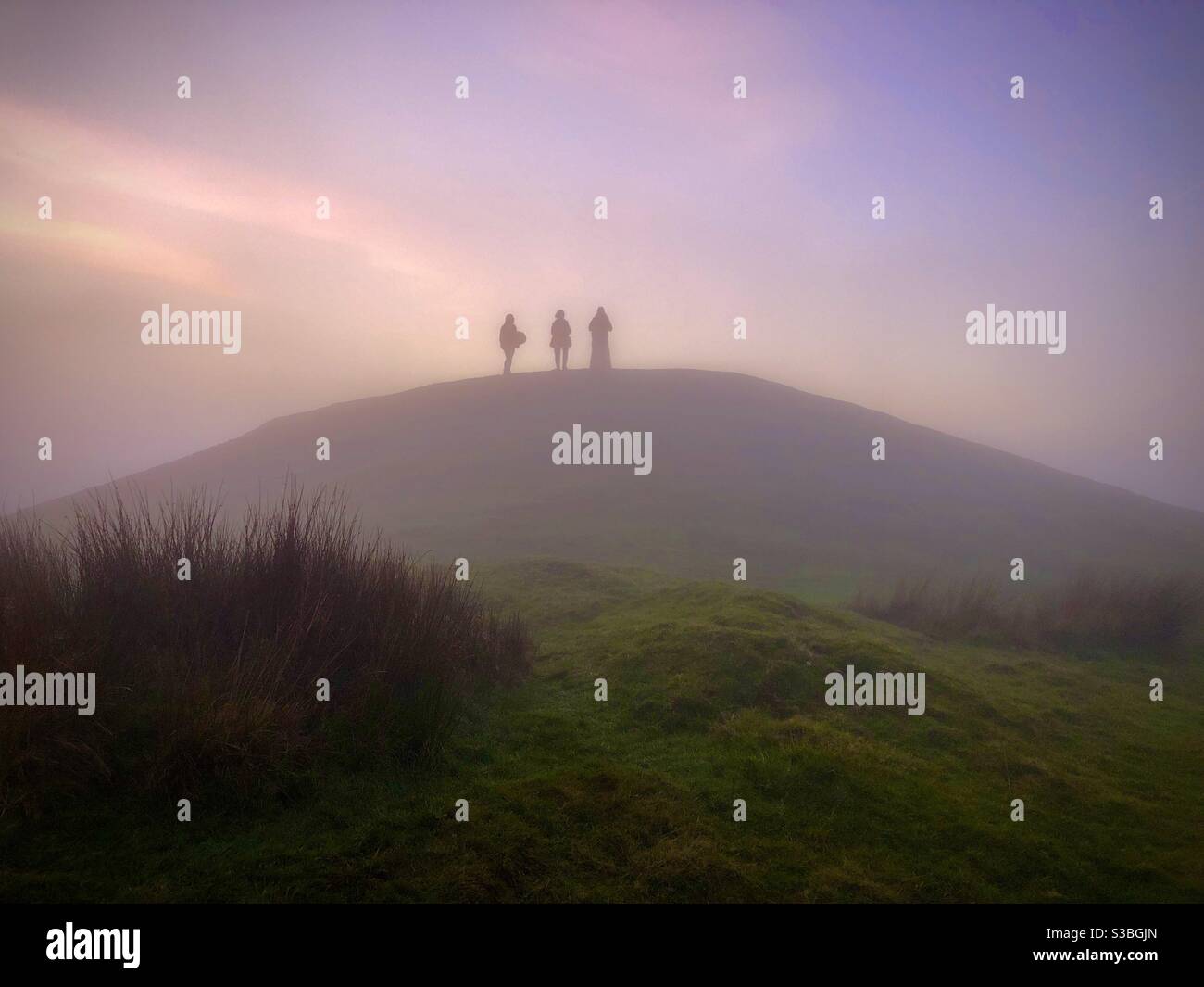Drei Figuren auf dem Gipfel des Garth Berg in der Abenddämmerung, Cardiff, South Wales, Ende November silhouetted. Stockfoto