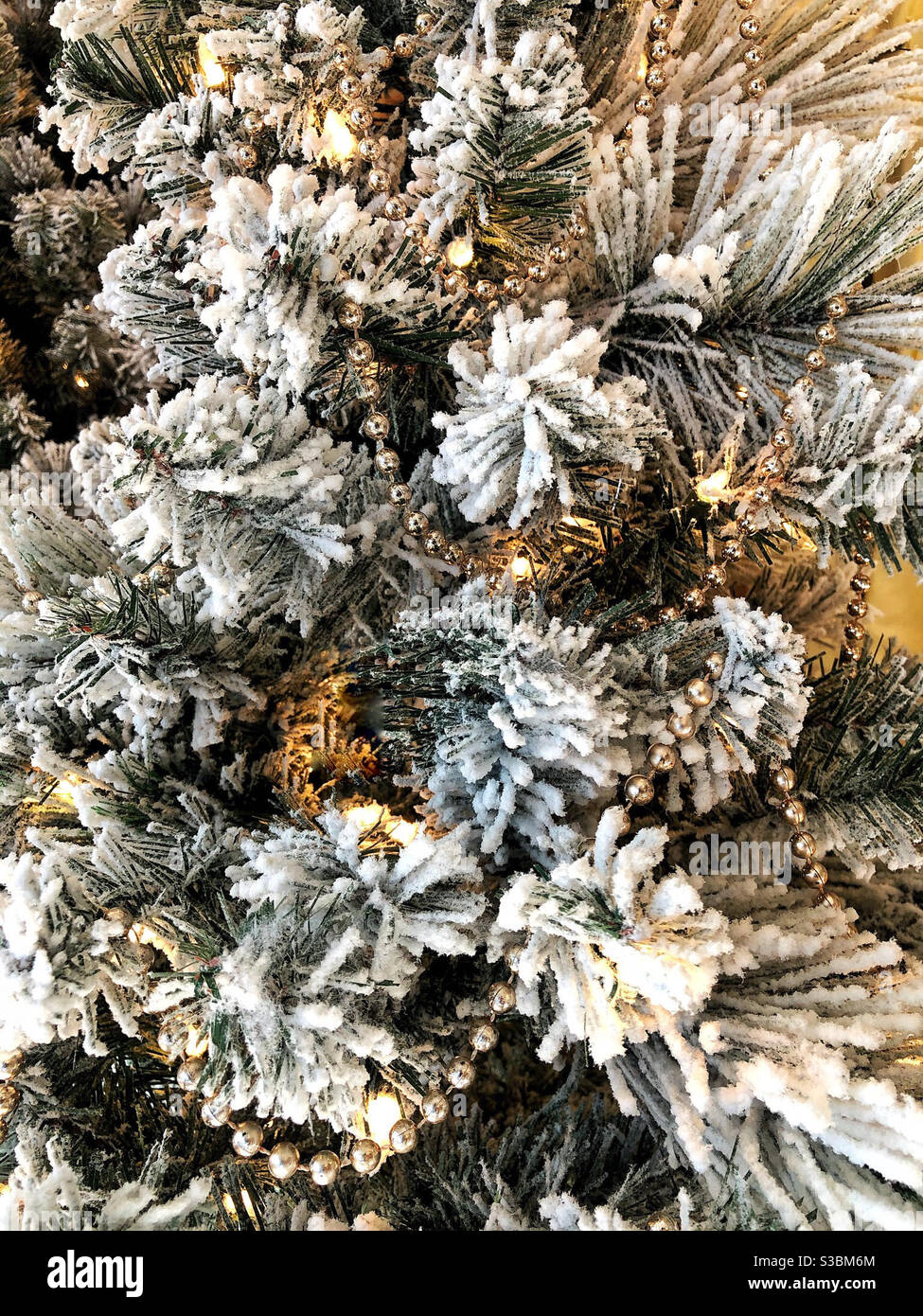 Weihnachtsbaum mit goldener Girlande, frostigen Schnee und Lichter geschmückt - Smartphone-aufgenommenes Stockfoto