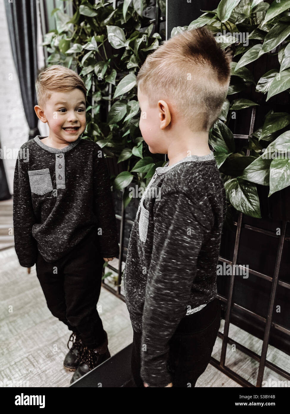 Blonde Junge lächelt auf seine eigene Reflexion, nachdem er seine Haarschnitt Stockfoto
