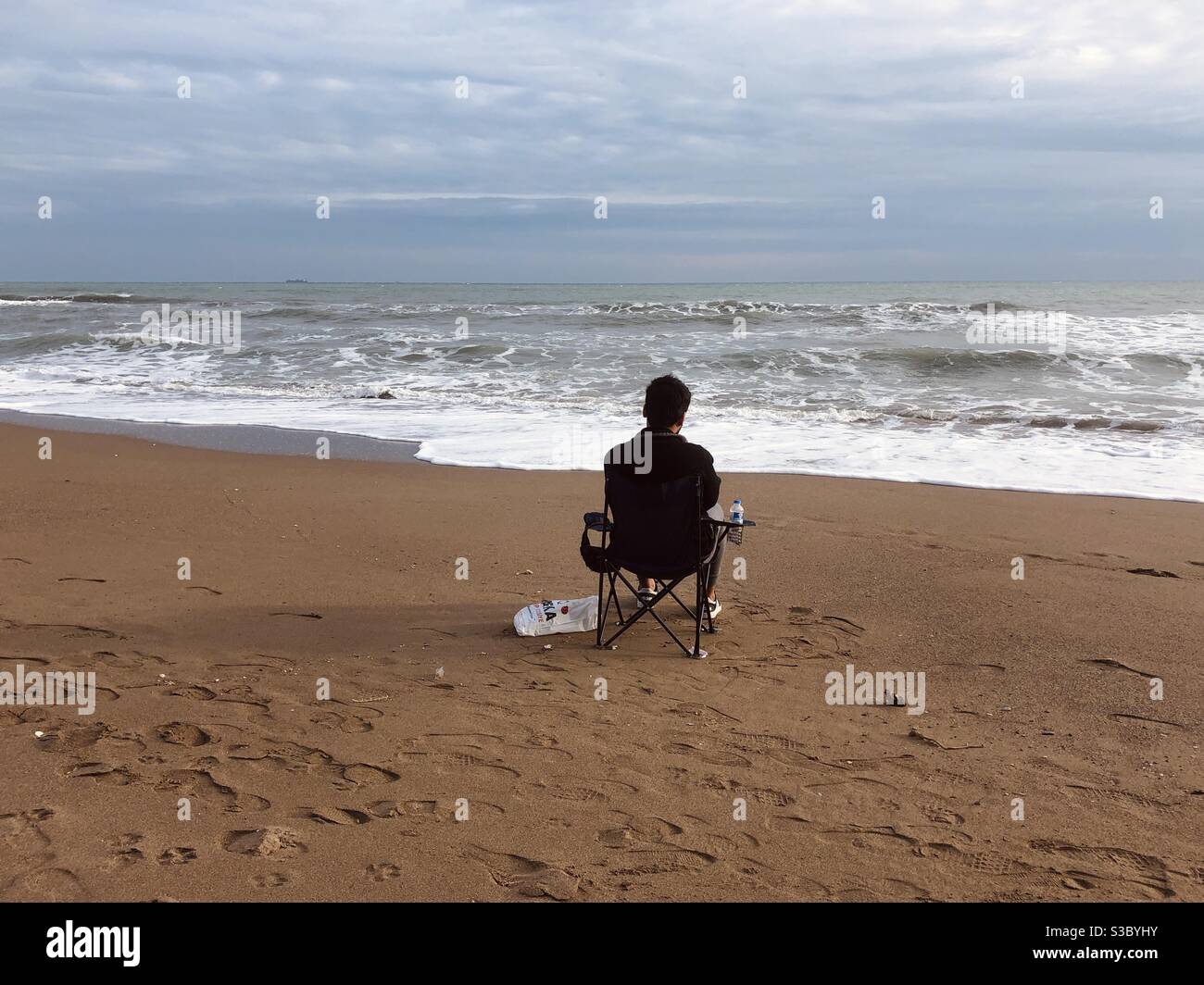 Mann sitzt auf einem Stuhl am Strand Stockfoto