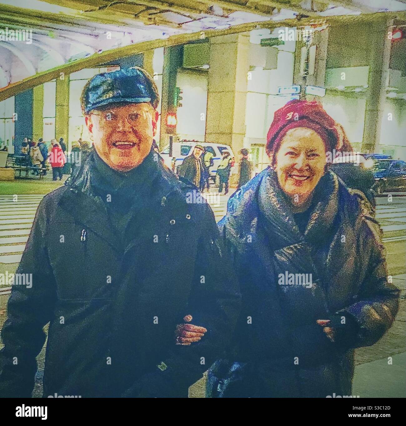 Lächelndes Paar, das Arm in Arm in Arm in einer kalten Winternacht auf der 42nd Street & Oark Avenue, NewYork City, USA, spazieren geht. - Smartphone-aufgenommenes Stockfoto