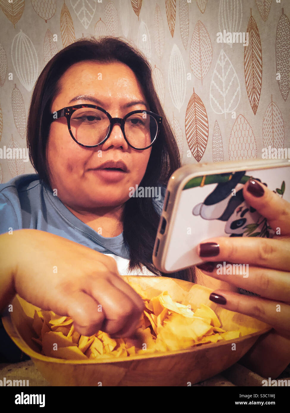 Eine Frau, die Snacks isst, während sie sich einen Film auf ihrem Smartphone ansieht. - Smartphone-aufgenommenes Stockfoto