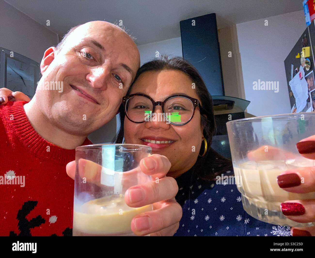 Ein gemischtes Rennpaar nimmt zu Weihnachten ein Selfie mit festlichen Getränken in der Hand. - Smartphone-aufgenommenes Stockfoto