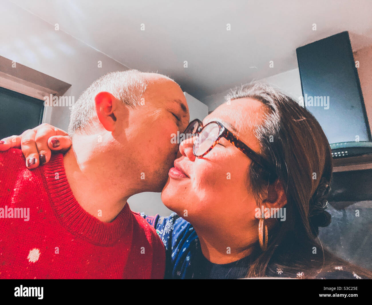 Ein gemischtes Rennpaar teilt sich einen Kuss auf die Wange. - Smartphone-aufgenommenes Stockfoto