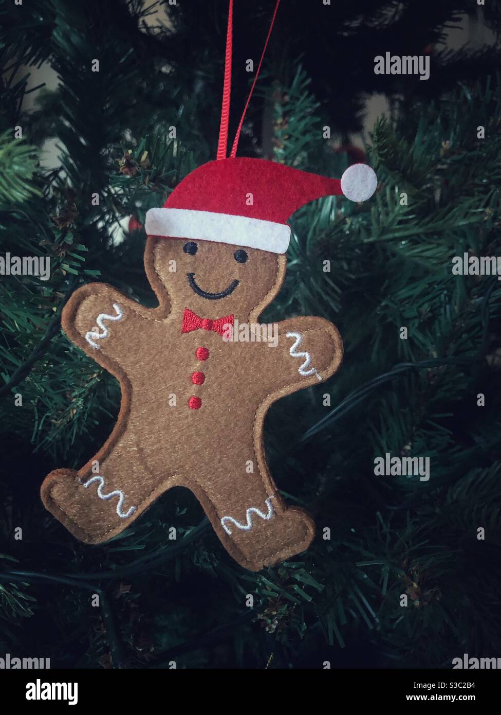 Ein glücklicher Lebkuchen Mann oder Person Weihnachtsbaum Dekoration hängen Auf einem Weihnachtsbaum mit Weihnachtsmann Hut auf - Smartphone-aufgenommenes Stockfoto