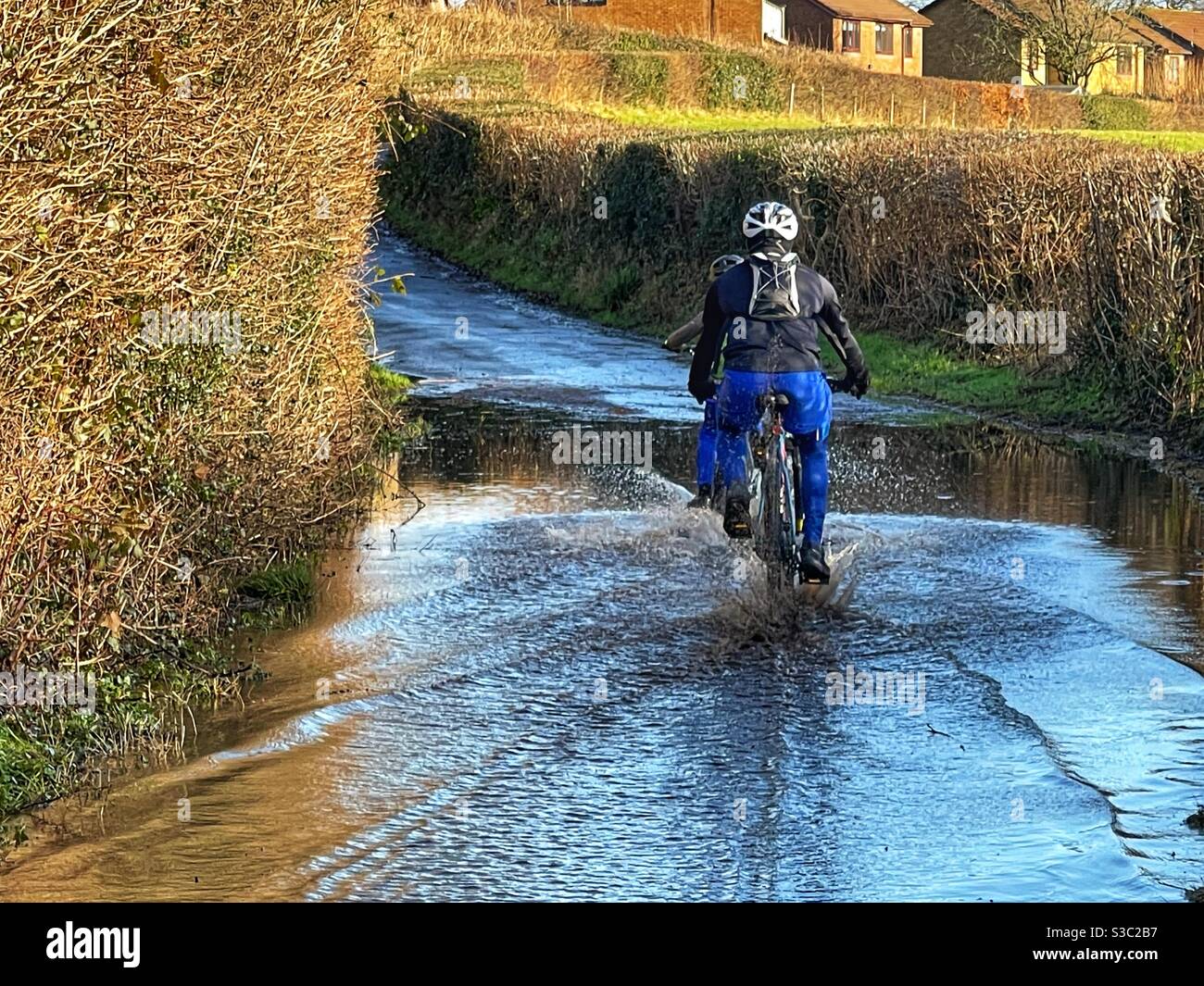 Menschen, die durch Hochwasser auf einer schmalen Landstraße radeln - Smartphone-aufgenommenes Stockfoto
