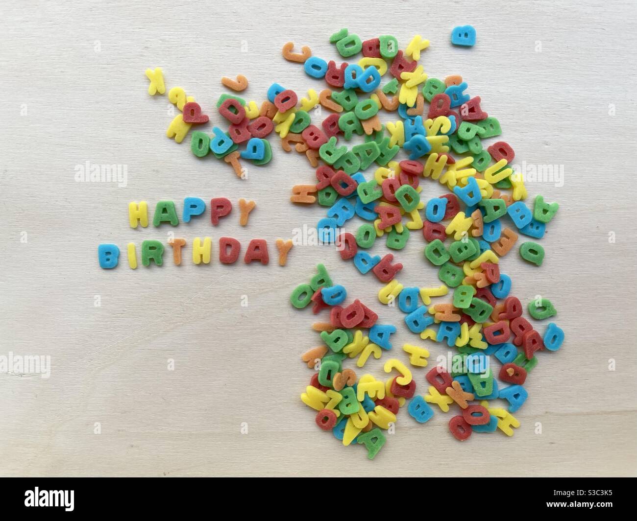 Happy Birthday Phrase mit ornamentalen mehrfarbigen Zucker Buchstaben komponiert Über einem Holzbrett Stockfoto