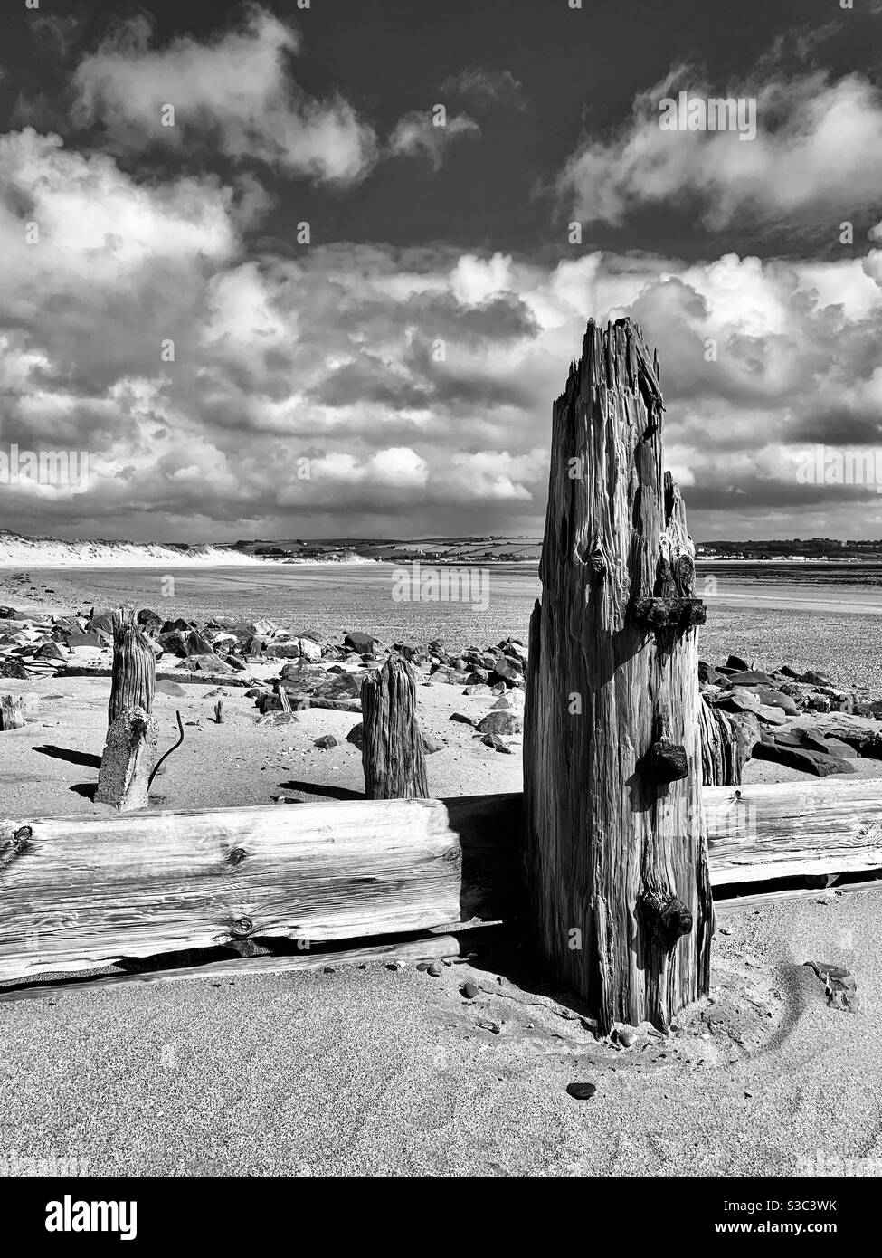 Sandgestrahlter verwitterter Holzpfosten mit rostigen Eisennägeln zwischen Felsen am Strand von Crow Point, Nord-Devon Küste, mit dramatischem Himmel an einem Sommertag 2020 Stockfoto