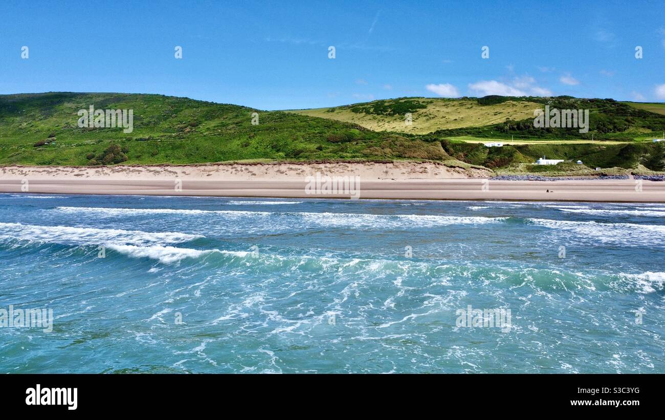 Drohne aus dem Meer von Woolacombe Strand, Nord Devon, England. Rollende blaue Wellen in Richtung verlassenen Sandstrand mit Gras bedeckten Sanddünen in der Ferne. Sommer 2020 Stockfoto