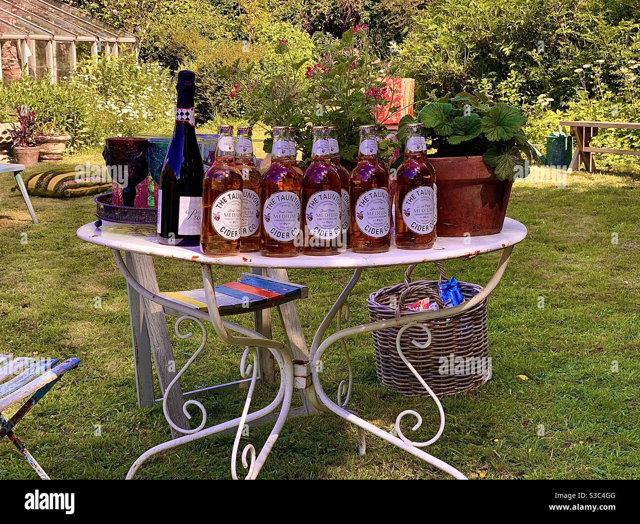 Englische Sommer Gartenparty mit Flaschen Apfelwein auf vintage Gartentisch aus Metall im Schatten Stockfoto