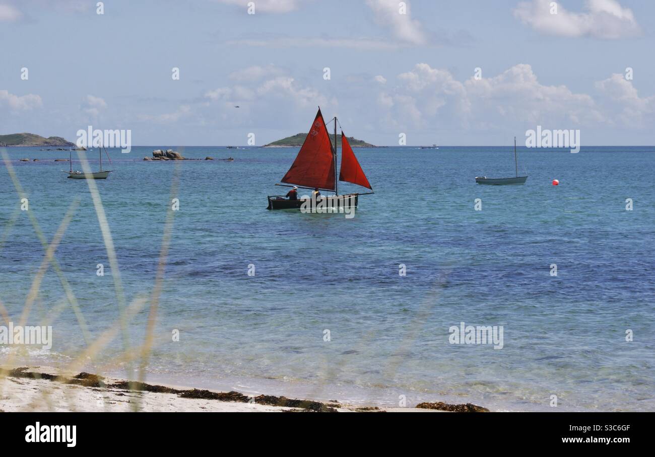 Kleines Segelboot mit roten Dreieckssegeln auf flachem Atlantik vor den Scilly Inseln im Sommer, England, UK Stockfoto