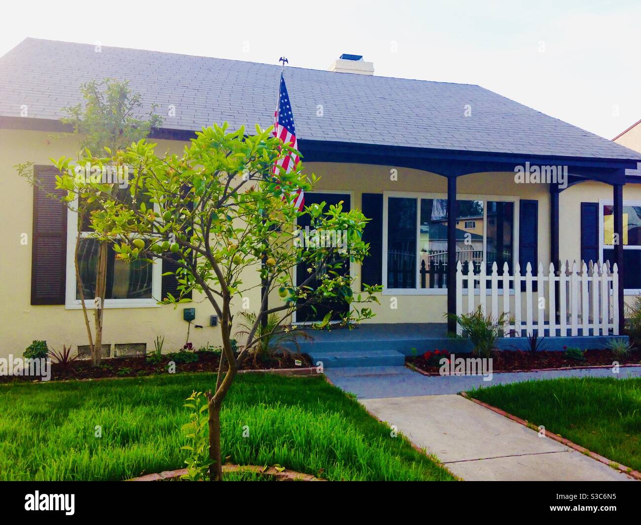 Ikonisches vorstädtisches Mittelklassehaus, erbaut in den 1940er Jahren im San Fernando Valley von Los Angeles, Kalifornien, USA mit einem weißen Zaun und amerikanischer Flagge - Smartphone-aufgenommenes Stockfoto